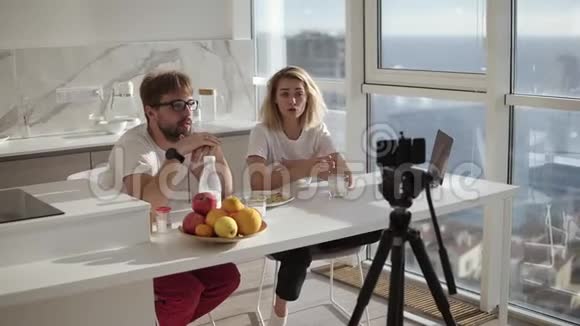 年轻的幸福夫妇博主和镜头聊天一边吃早餐一边在镜头上录制视频聊天对着镜头说话视频的预览图