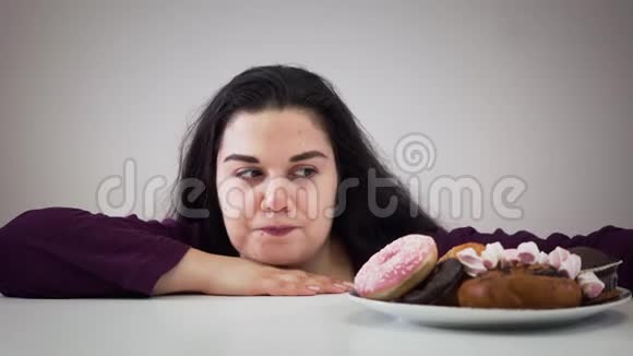肥胖的白种人黑发女孩从盘子里拿甜点和咀嚼的肖像有趣的胖女人吃糖果视频的预览图