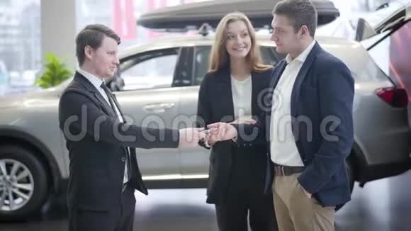 侧面的男性白种人汽车经销商给予钥匙从新的车辆到快乐的业主摇动的人他的手视频的预览图