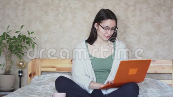 年轻迷人的女孩在家坐在床上远程工作视频的预览图