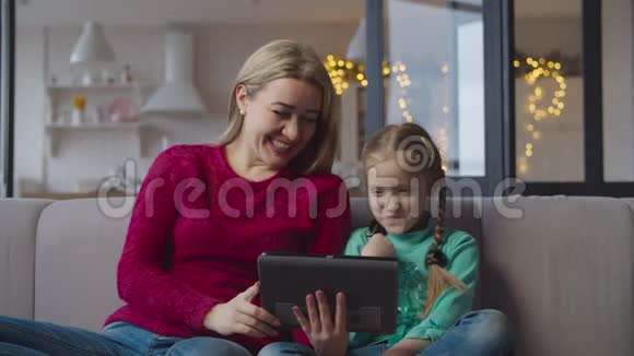 沙发上的母亲和女孩与平板电脑联网视频的预览图