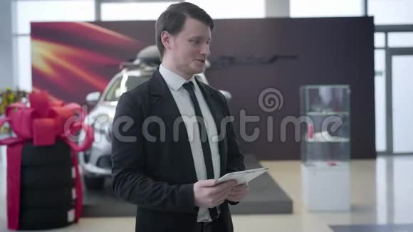 白种人微笑汽车经销商欢迎客户在展厅的肖像成功的商人来到汽车经销店视频的预览图