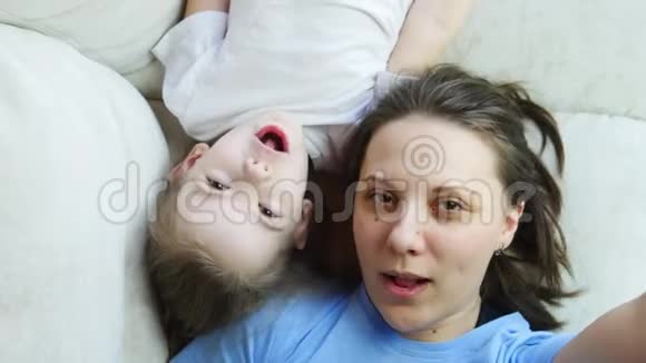 年轻的妈妈和孩子躺在床上玩自拍视频的预览图
