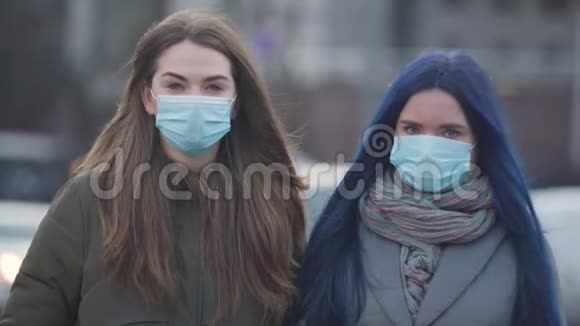两个戴着防护面具的女人站在城市街道上看镜头的肖像年轻女性朋友视频的预览图