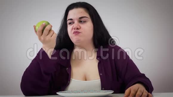 沮丧的年轻白人胖女孩吃苹果胖女人把水果放在一边看着远处自我控制节食视频的预览图