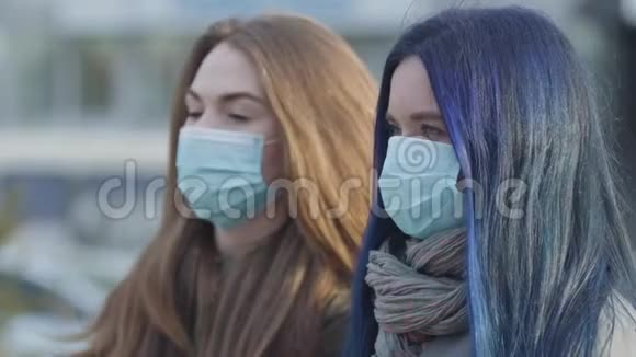 侧视特写两个焦虑的女人戴着防护面具看着远处站在城市街道上的女人重点变化视频的预览图