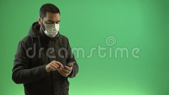 在绿色背景下智能手机上戴防护面罩的男人视频的预览图