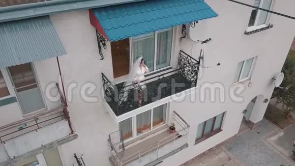 身着晚礼服的新娘站在她家的阳台上结婚的早晨空中景观视频的预览图