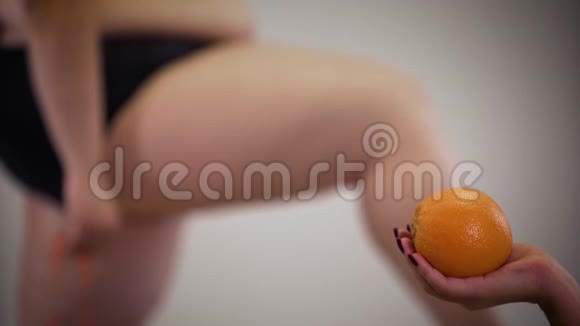 无法辨认的白种人肥胖妇女用卷尺测量肥胖的腿背景是女性手握橙色视频的预览图