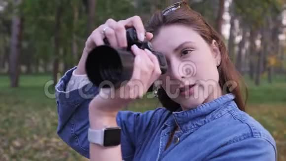 一个女人在一个美丽的秋天公园的背景下用黑色紧凑型相机拍照静态宽镜头视频的预览图