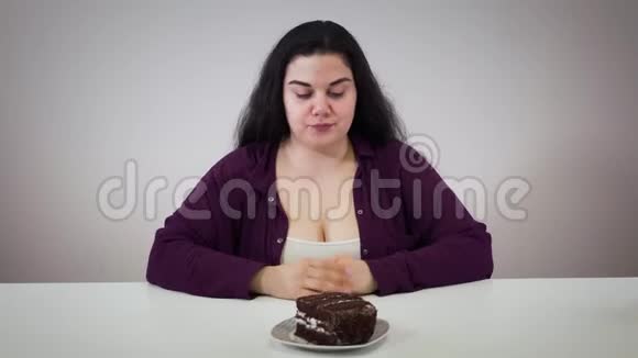 年轻的白人丰满的女孩闻着巧克力蛋糕把糖果移到一边头发花白的女人控制自己视频的预览图