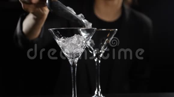 冰块缓慢地落入空玻璃中快关门女酒保在黑暗背景下做鸡尾酒视频的预览图