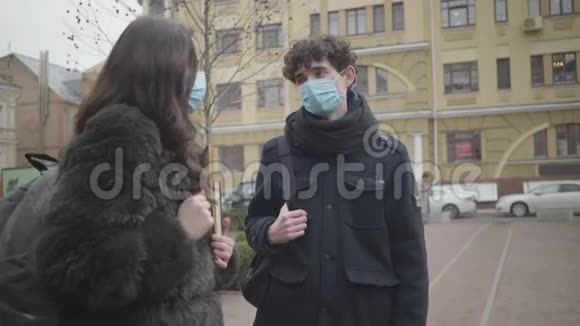 两名戴防护面罩的大学生在城市街道上交谈认真负责的男孩和女孩在户外聚会视频的预览图