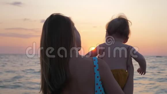 母亲抱着婴儿看着海边或海边的日落视频的预览图