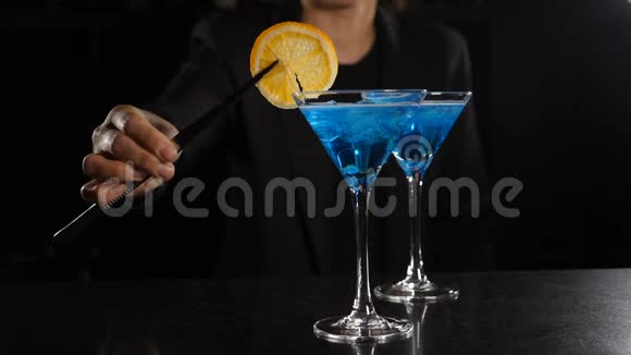 准备好的鸡尾酒在夜总会的酒吧里女调酒师用蓝色液体和柠檬片装饰鸡尾酒视频的预览图