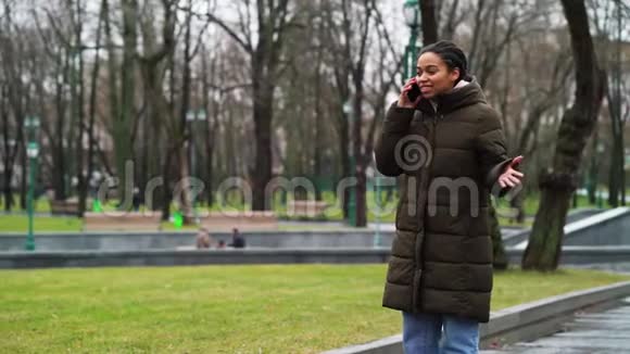阳光明媚的黑人女孩在枯燥的天气里在公园里打电话视频的预览图