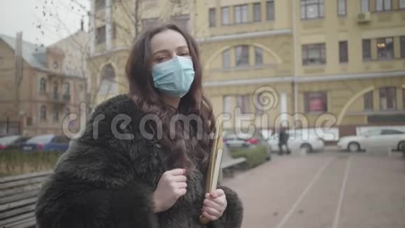 美丽的白种人黑发女人戴着面具站在城市街道上拿着书的肖像有意识的公民视频的预览图