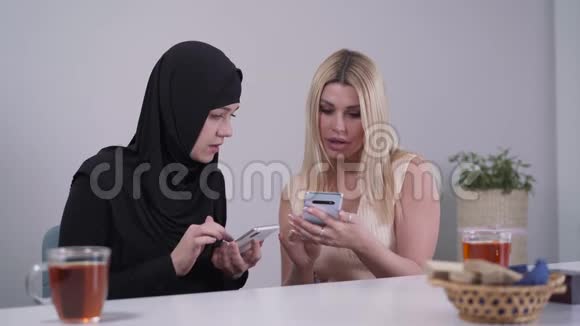 两位来自不同文化的年轻女性在智能手机上使用社交媒体穆斯林和高加索女人坐在视频的预览图