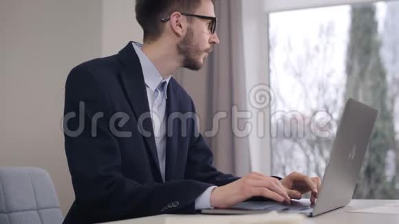 年轻英俊的白种人的肖像看着窗外在笔记本电脑键盘上打字自信的商人视频的预览图
