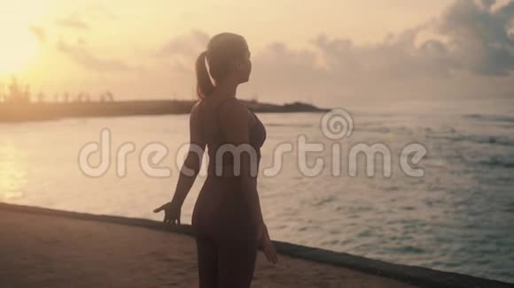 女人练习伸展运动的剪影海滩日出时的瑜伽慢动作视频的预览图