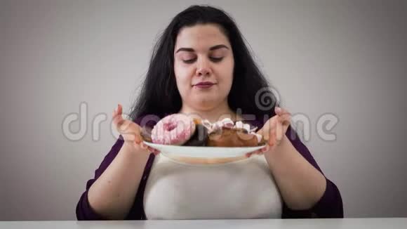 饥饿的白种人胖女人拿着盘子和糖果和闻甜点的肖像奥比斯女孩贪婪地看着视频的预览图
