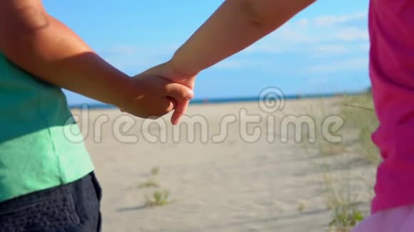 穿着粉红色裙子的小男孩和小女孩在海滩上牵手视频的预览图