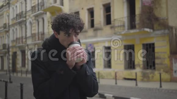 年轻的黑发白种人卷发在外国城市四处张望喝着咖啡男性游客视频的预览图