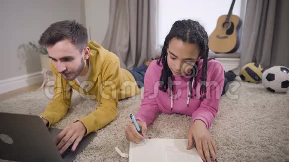美国黑人女孩专心写作把手放在地板上白人男孩抚摸着她的手掌微笑着视频的预览图