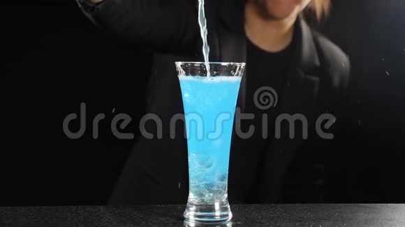 女调酒师在黑色背景下做蓝色冰鸡尾酒酒吧老板把明亮的蓝色酒倒入装满玻璃的玻璃中视频的预览图