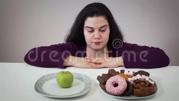 一幅深谋远虑的黑种人白种人女人看苹果和糖果盘子的肖像肥胖女孩选择视频的预览图