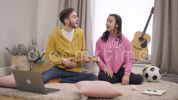 热情的白种人男孩玩四弦琴和女非裔美国朋友唱歌快乐的年轻朋友视频的预览图