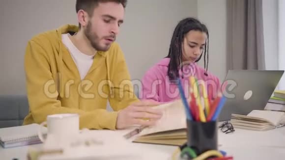 镜头向上移动两个年轻的队友坐在桌子旁学习白种人疲惫的男孩打哈欠和精疲力竭视频的预览图