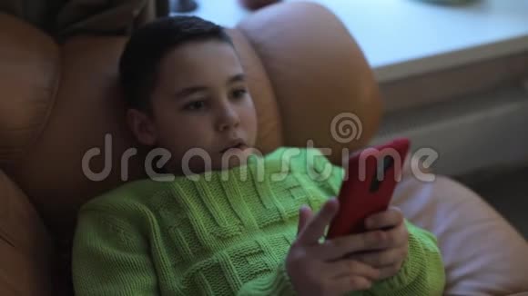 穿着绿色套头衫手机躺在沙发上的男孩视频的预览图