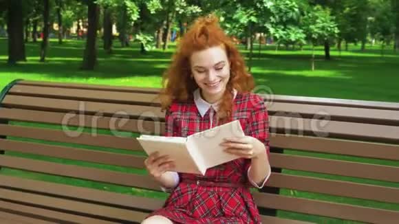 在绿色公园读有趣的书的漂亮女孩视频的预览图