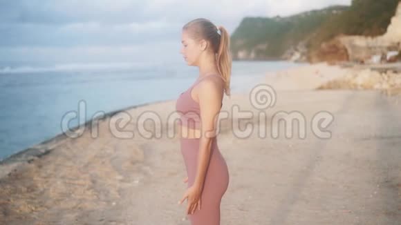 年轻女性练习瑜伽在海滩上做伸展运动慢动作视频的预览图
