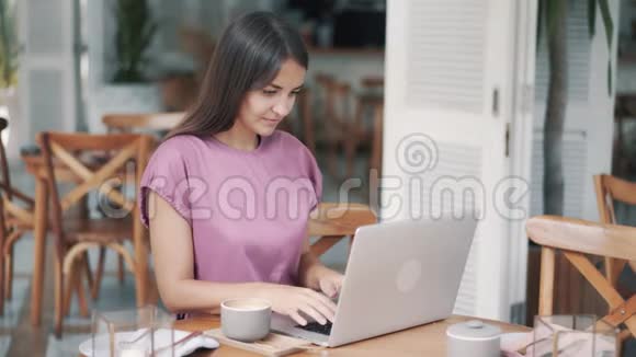 美丽的年轻女性自由职业者喝咖啡用笔记本电脑在咖啡馆工作视频的预览图