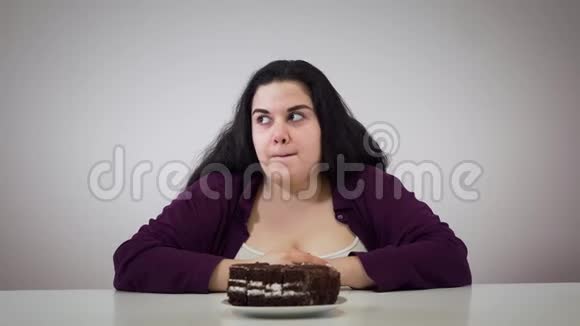 深色头发的胖女孩四处张望咬着一块巧克力蛋糕的肖像有超重问题的白人女性视频的预览图