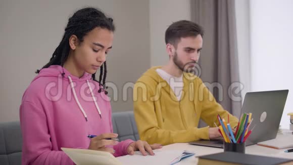 年轻的非裔美国女孩和白人男孩坐在桌子旁学习的肖像男人用笔记本电脑女人视频的预览图