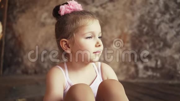 悲伤的小可爱的女婴头上戴着蝴蝶结盘腿坐在地板上在斯泰迪加姆上射击关门视频的预览图