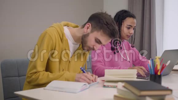 欢快的学生坐在桌子旁学习的画像非洲裔美国女孩与白人男孩和视频的预览图