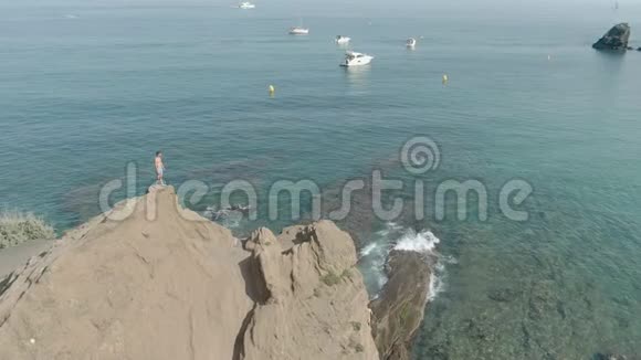 一个年轻人站在清澈的海面上的悬崖上视频的预览图