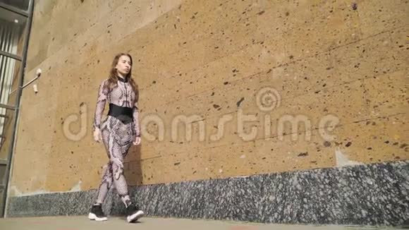 穿着运动服的漂亮年轻运动女孩优雅地沿着棕色的混凝土墙走慢动作对斯泰迪达姆的射击视频的预览图