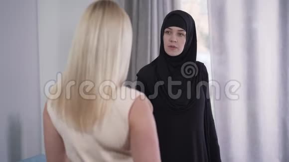 对金发白种人女人与穆斯林朋友讨论时尚的看法年轻谦虚的女人戴着头巾视频的预览图