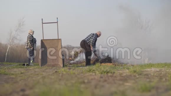 一个成熟的白种人男人当他的高级妻子站在一边时把落叶扔进火里农村农民视频的预览图