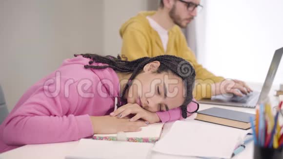戴眼镜的年轻白种人男孩唤醒了非裔美国人的伴侣疲倦的学生睡在桌子旁视频的预览图
