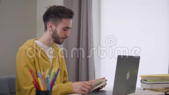 侧面观看自信的白种人男孩坐在桌子前和视频聊天年轻英俊的学生用笔记本电脑视频的预览图