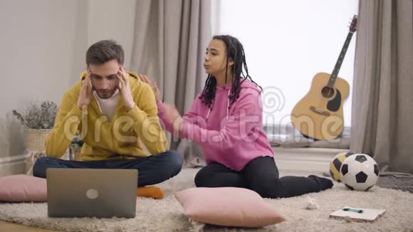 紧张的白人年轻人坐在笔记本电脑前双手抱着头听音乐的画像视频的预览图