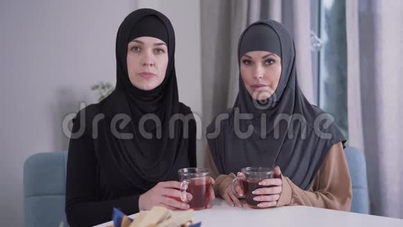 两个自信的女人戴着头巾看着镜头微笑的肖像在室内摆姿势的时髦女士视频的预览图
