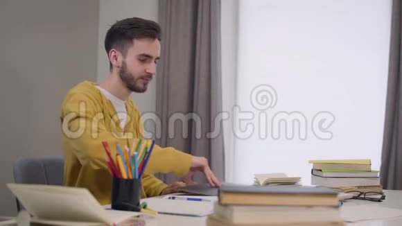年轻的黑发白种人男孩打开笔记本电脑的肖像挥手和微笑自信男学生视频聊天视频的预览图