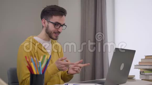 英俊自信的白种人男孩戴着优雅的眼镜坐在桌子旁视频聊天男性学生视频的预览图